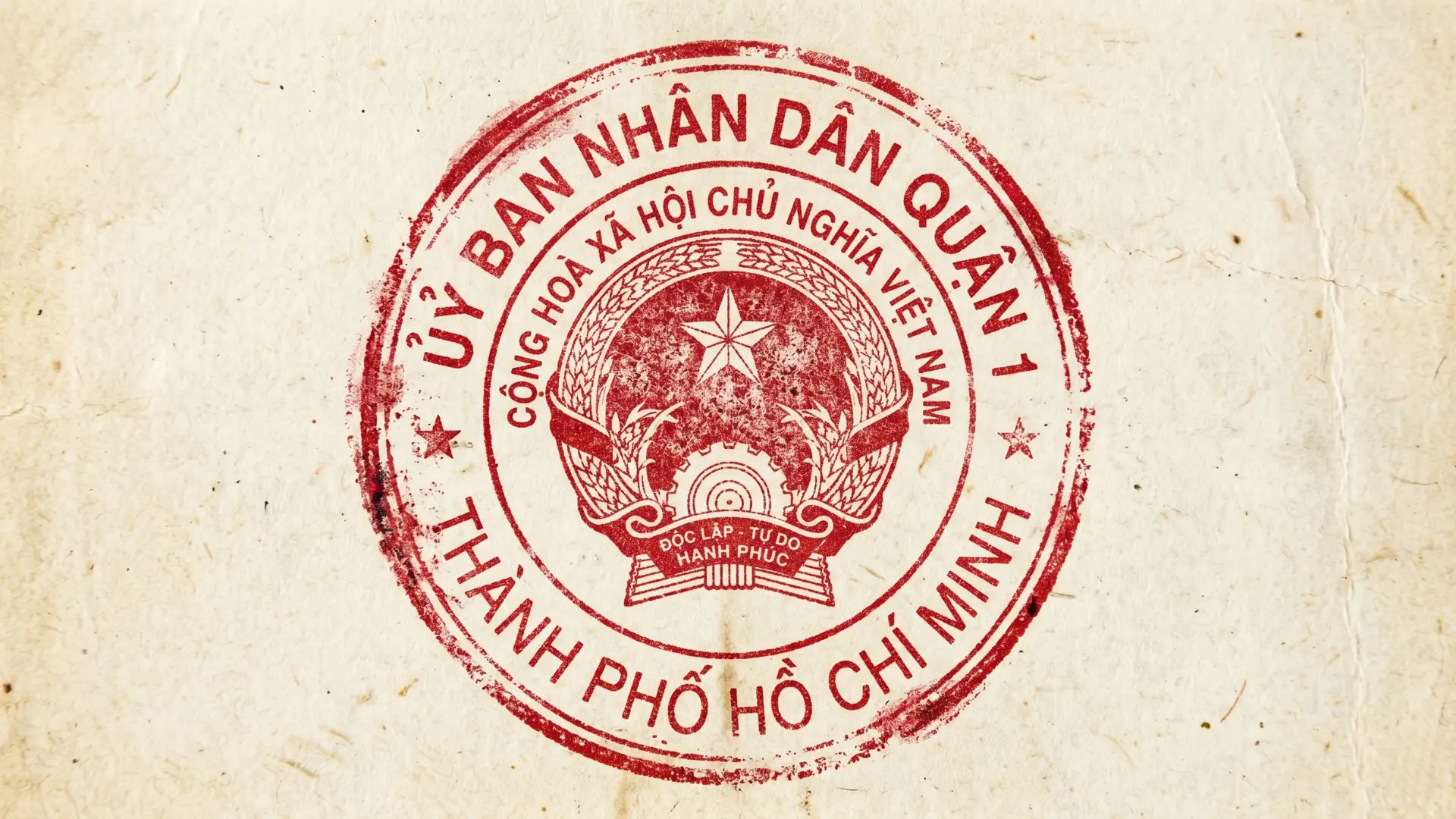 Red circular official seal on beige textured paper featuring Vietnam’s national emblem: five‑pointed star above cogwheel and rice branches. Surrounding Vietnamese text identifies People’s Committee of District 1, Ho Chi Minh City.