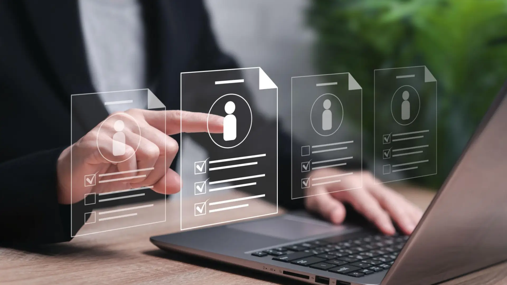 Person using laptop with transparent digital interface showing candidate profiles, icons, and checkboxes, representing recruitment or hiring process.