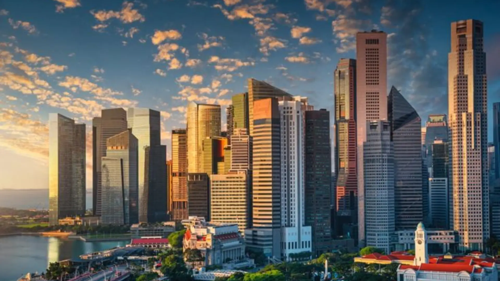 Vibrant city skyline with modern skyscrapers and historic buildings with red‑tiled roofs, clock tower in foreground, dramatic sky with warm light at sunrise or sunset.