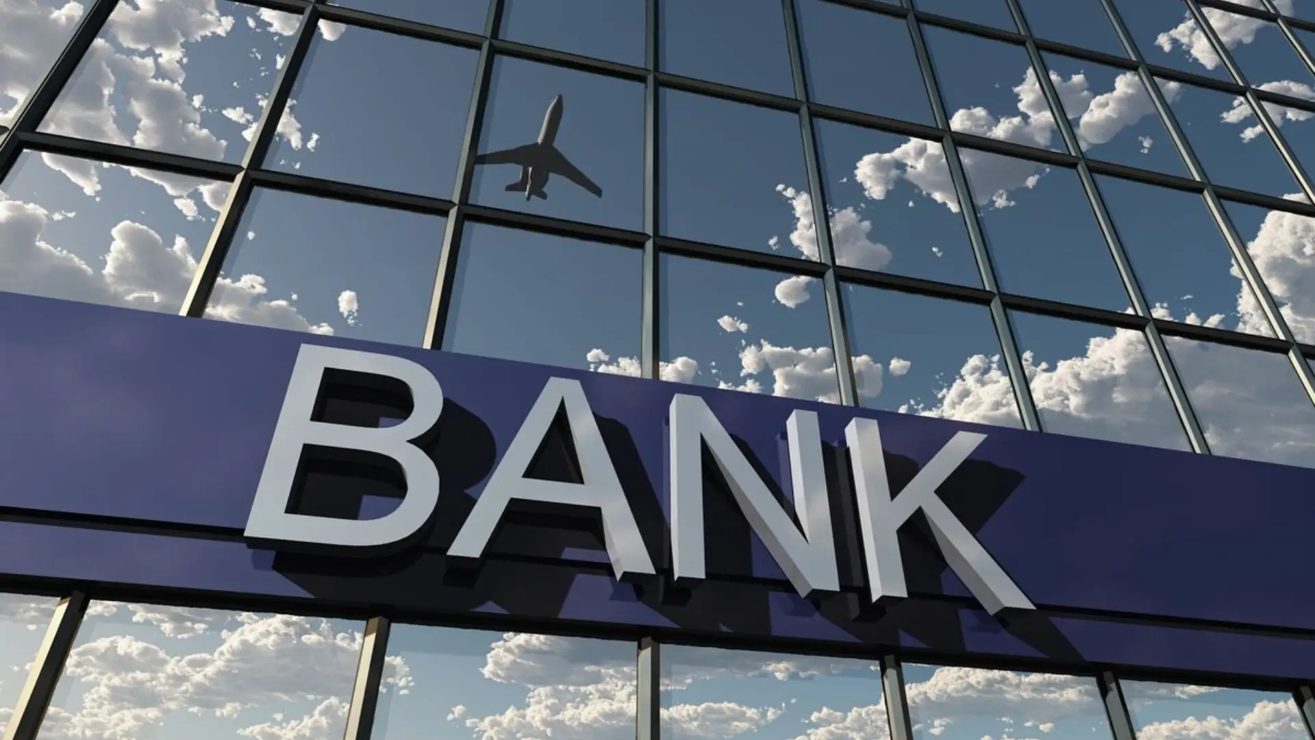Exterior of modern bank building with large “BANK” sign on glass facade reflecting sky and silhouette of airplane, symbolizing global finance and mobility